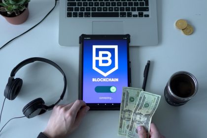 Tablet com representação de tecnologia blockchain, dinheiro em espécie e itens de escritório sobre uma mesa.