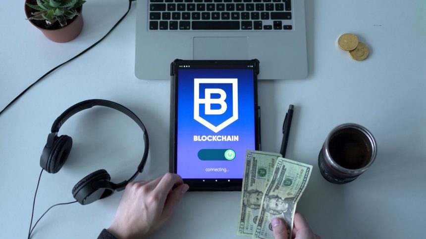 Tablet com representação de tecnologia blockchain, dinheiro em espécie e itens de escritório sobre uma mesa.