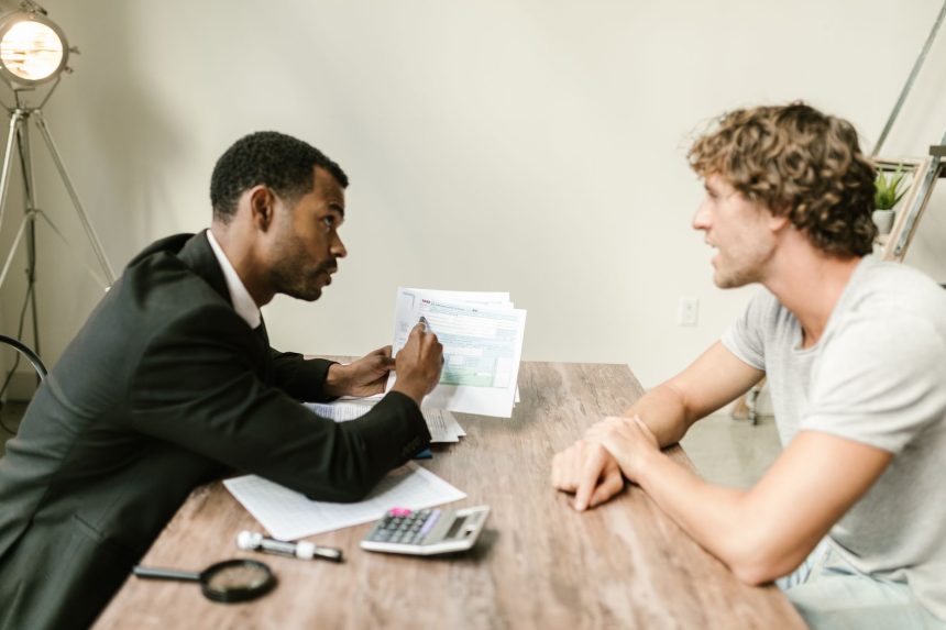 Consultor financeiro conversa com um cliente e analisa documentos em uma mesa de escritório.