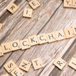 Peças de madeira formam a palavra “blockchain” sobre uma superfície rústica.