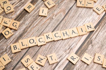 Peças de madeira formam a palavra “blockchain” sobre uma superfície rústica.