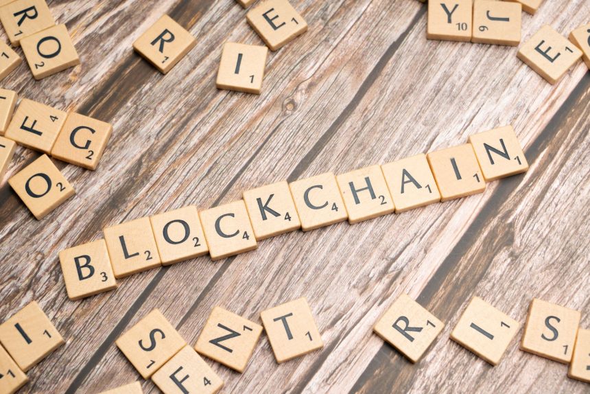 Peças de madeira formam a palavra “blockchain” sobre uma superfície rústica.